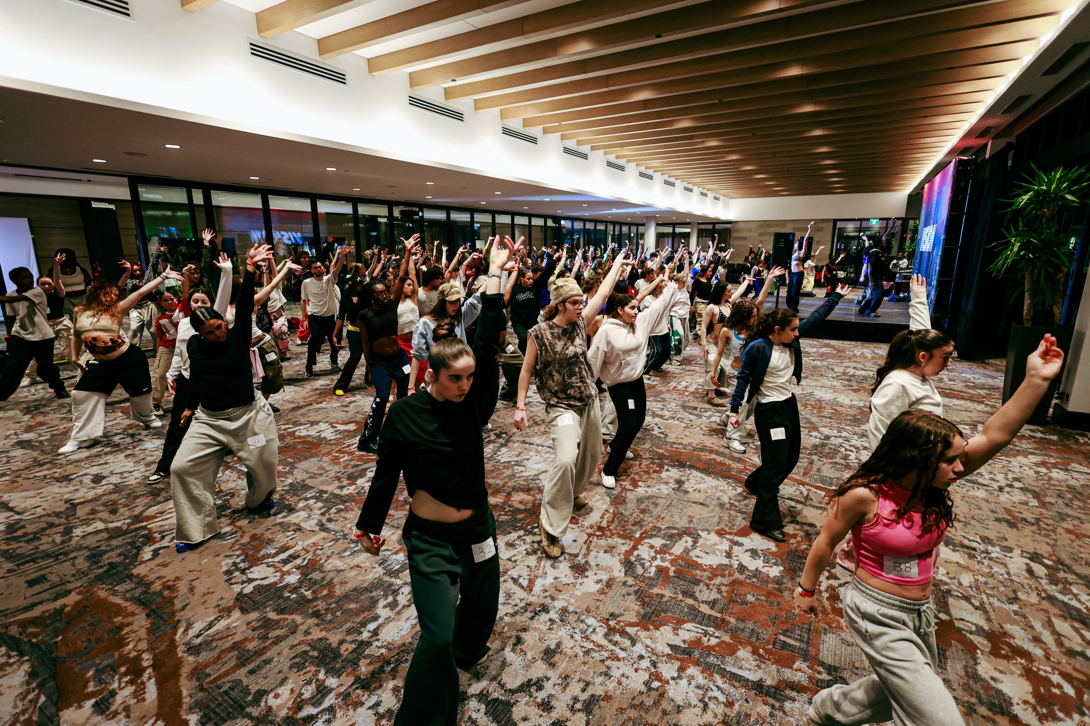 Wide angle scene of a packed workshop floor with dancers and audience members gathered around instructors.
